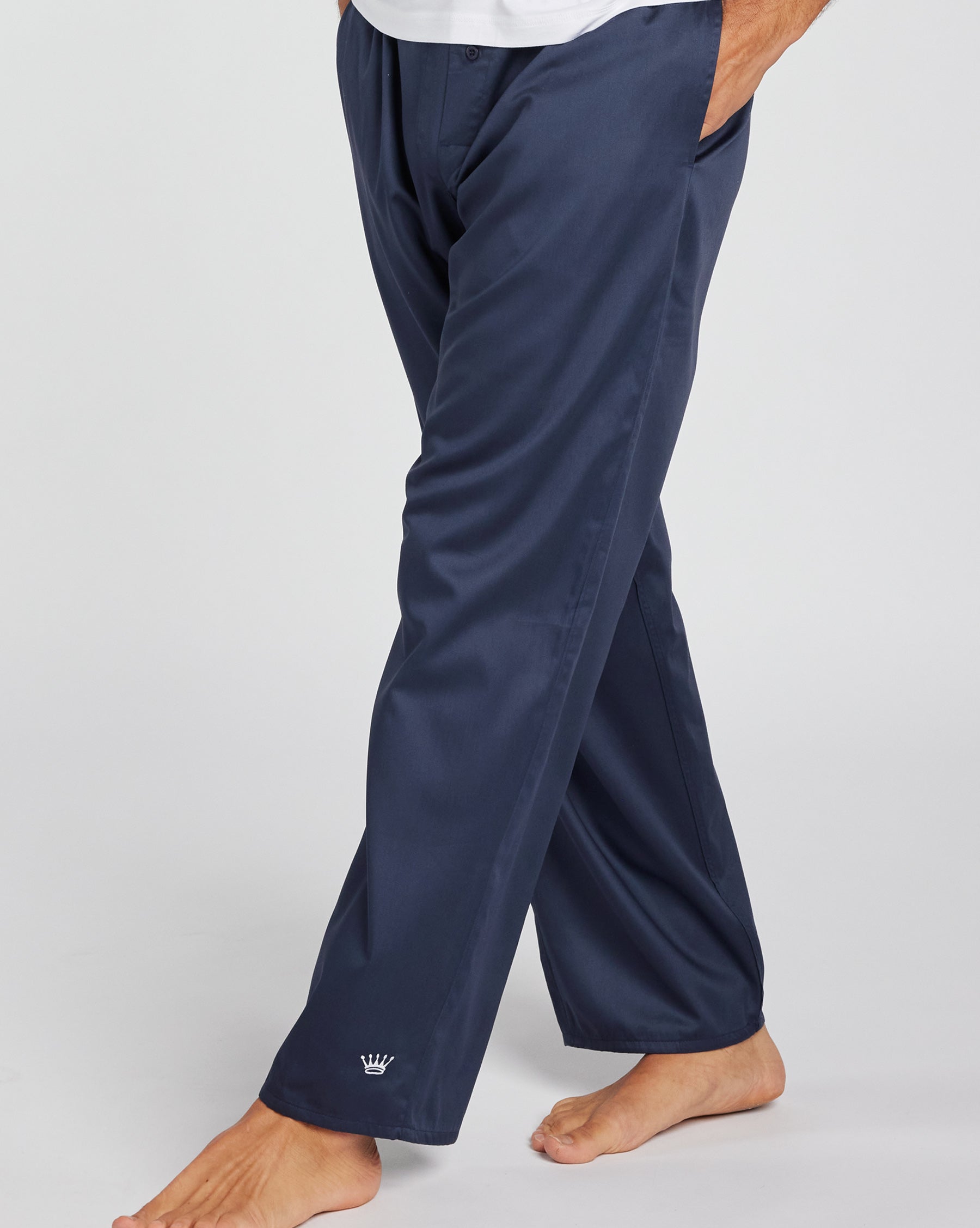 A person wearing navy blue lounge pants, shown from the waist down against a light gray studio background. The pants are loose-fit with a small white crown logo near the left ankle.