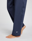 Close-up of a person wearing navy blue pants with a small white crown logo near the cuff, photographed against a light gray studio background.