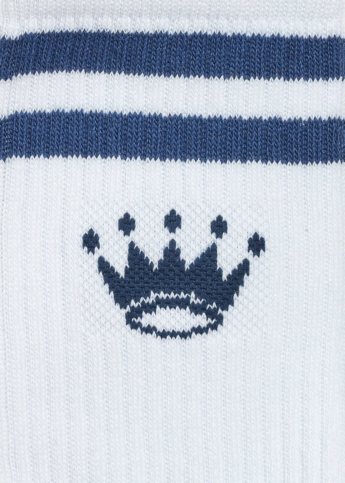 Close-up of a white knit sock with two horizontal navy blue stripes near the top and a navy blue crown motif centered below the stripes.