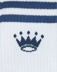 Close-up of a white knit sock with two horizontal navy blue stripes near the top and a navy blue crown motif centered below the stripes.
