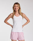 Woman wearing a white tank top and pink drawstring shorts, photographed against a clean light gray studio background.