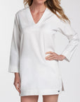 A woman wearing a white long-sleeve V-neck tunic-style top with a relaxed fit, shown against a plain light background.
